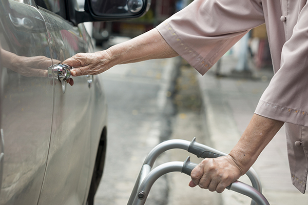 senior woman open car door with walker on street.